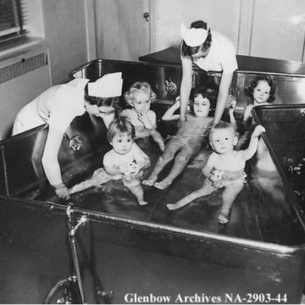 A black and white picture of two nurses practicing hydrotherapy on five young polio survivor in the hydro pool